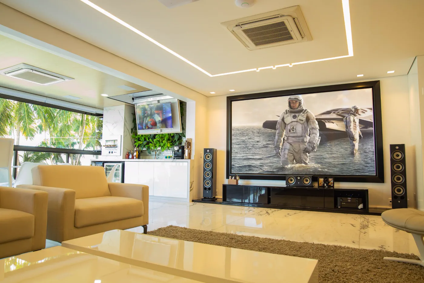 Sala de home theater com tela de projeção grande emoldurada, caixas acústicas torre e rack de equipamentos
