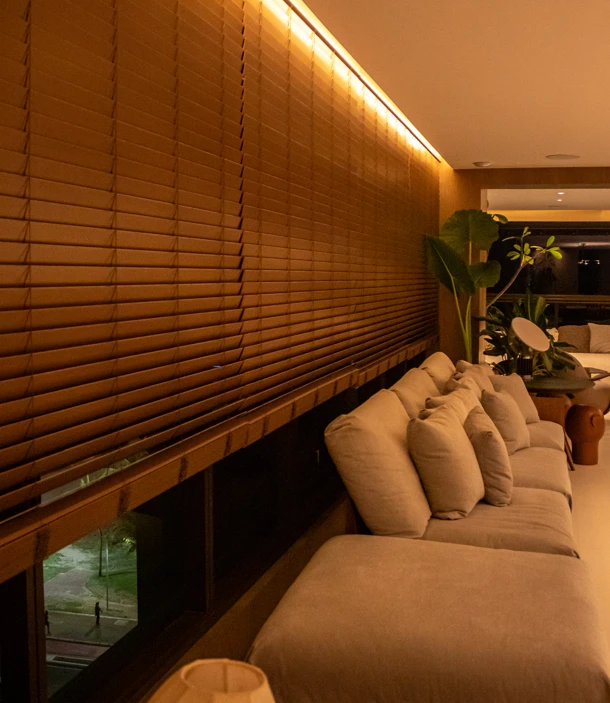 Persianas de madeira com iluminação embutida no teto e sofá claro em uma sala de estar