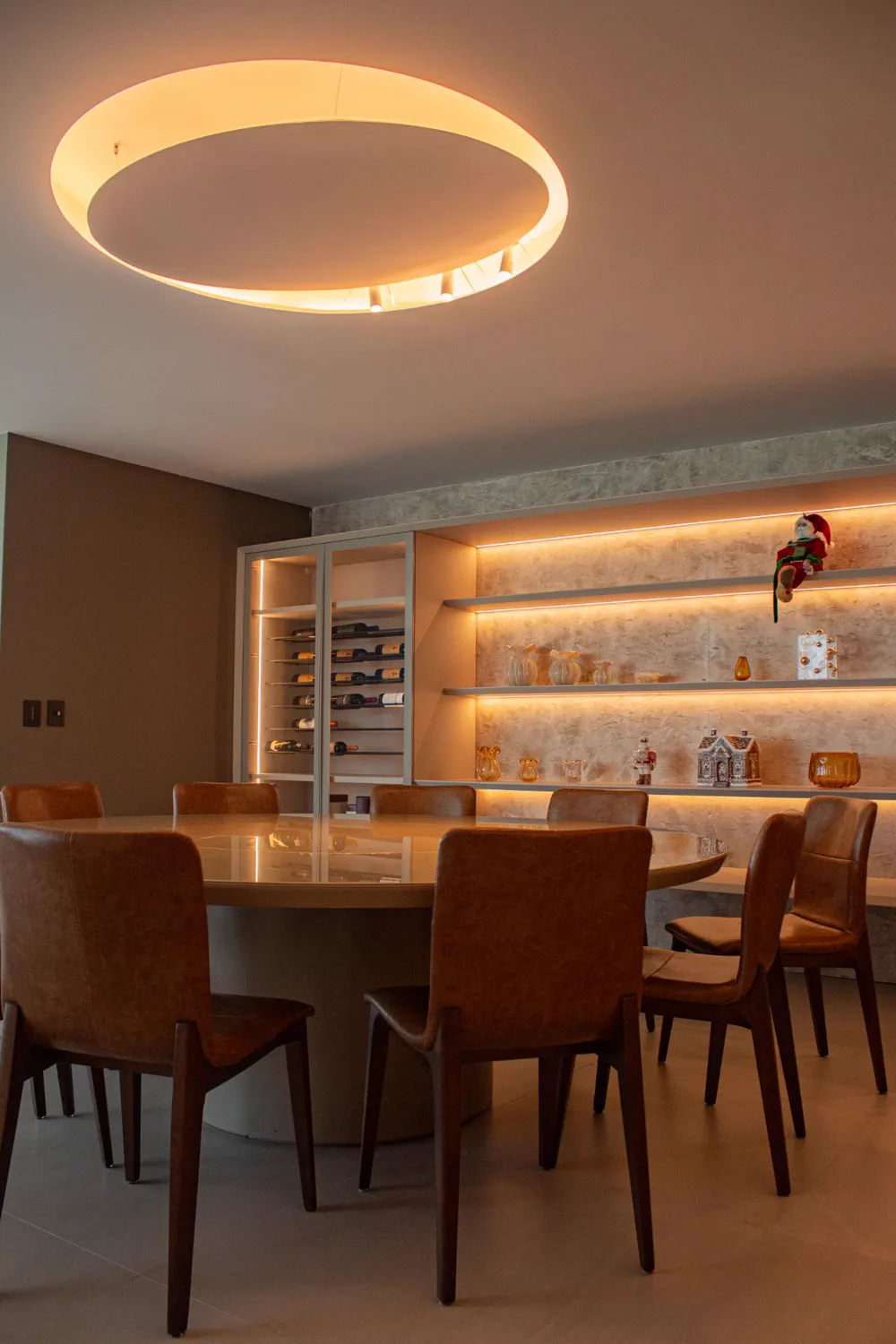Sala de jantar com luminária circular no teto e prateleiras com iluminação indireta