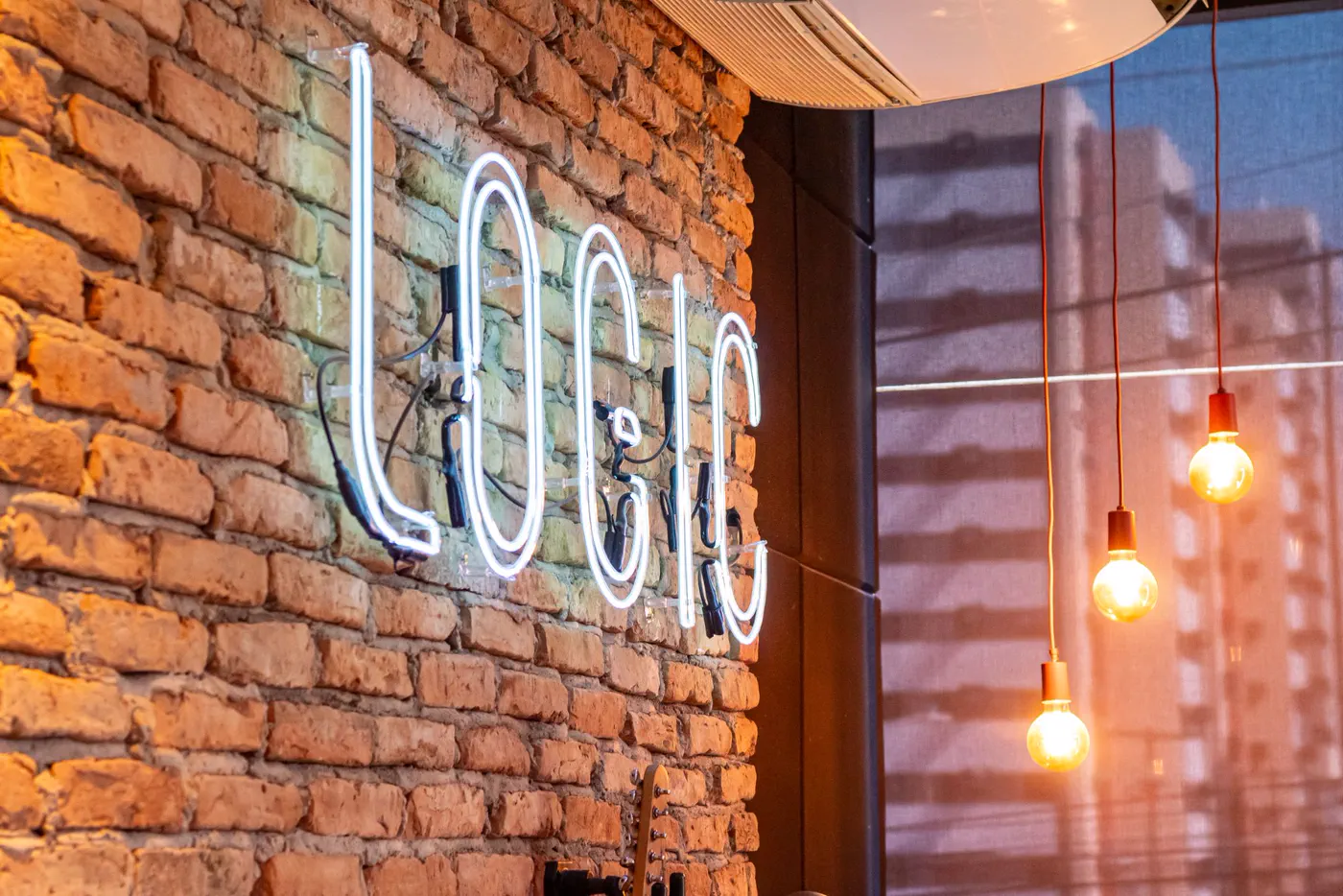 Letreiro de neon LOGIC em parede de tijolos aparentes no showroom, com lâmpadas pendentes